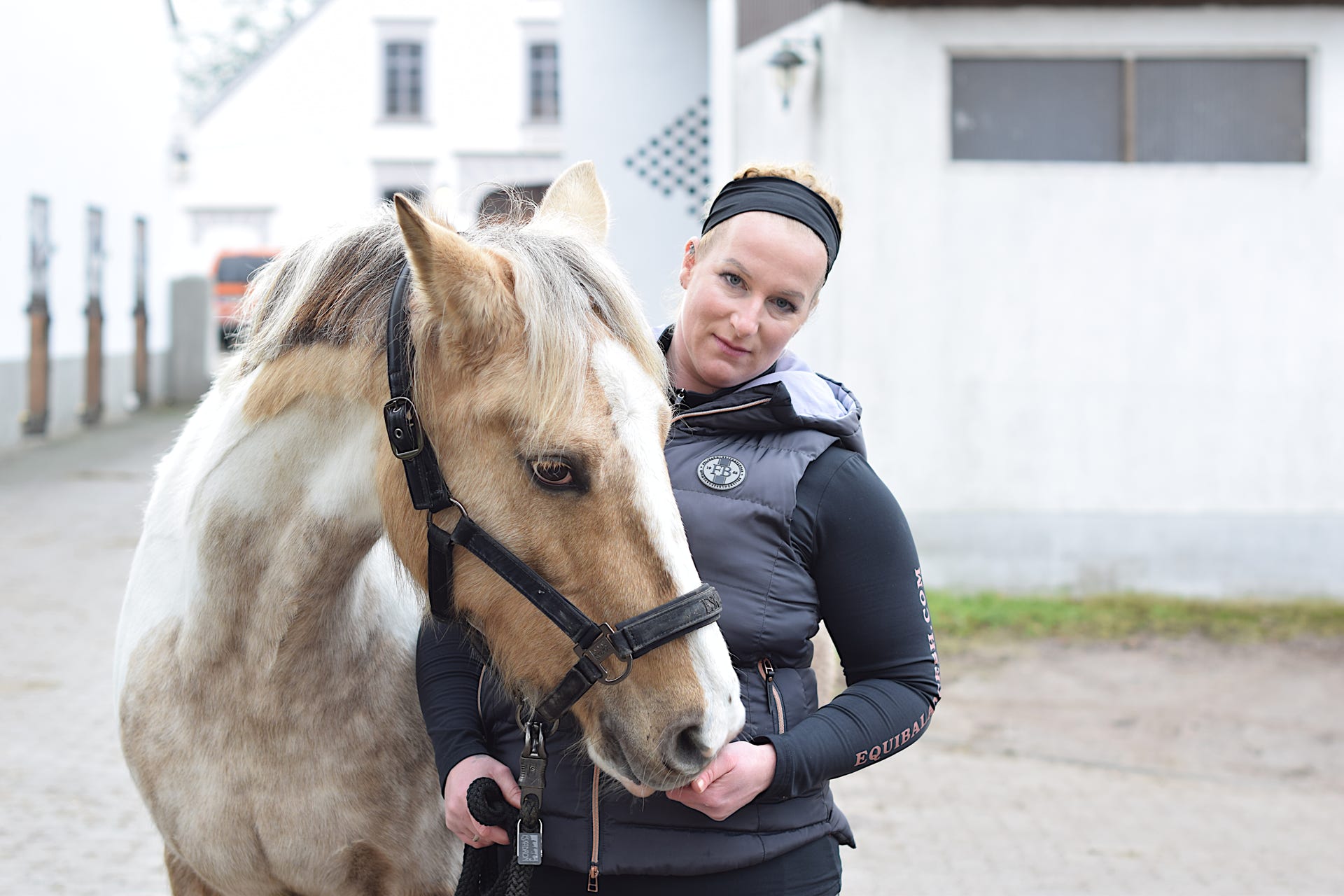 Pferdetherapeutin Sarah Hippe mit einem Pferd vor einem Gebäude.